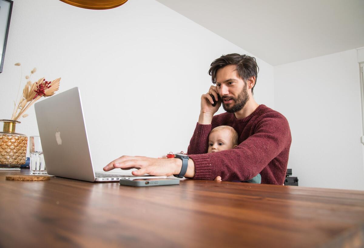 Ein Mann mit Baby sitzt vor einem Laptop.