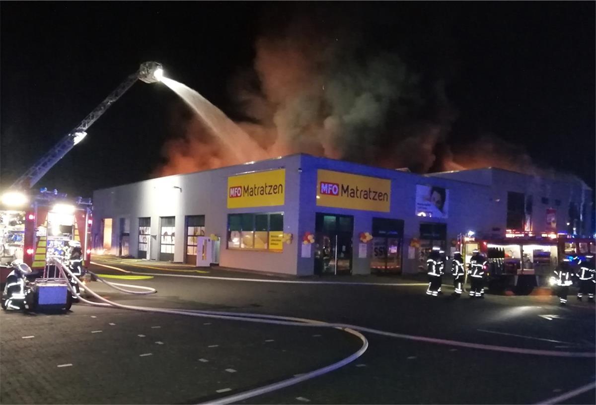 Lingen: Baumarkt geht in Flammen auf Qualm und Rauch über einem Gebäude in der Nacht. Feuerwehr mit Drehleiter löscht. Feuerwehrleute.
