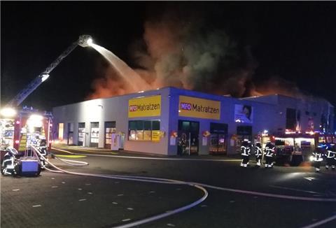 Qualm und Rauch über einem Gebäude in der Nacht. Feuerwehr mit Drehleiter löscht. Feuerwehrleute.