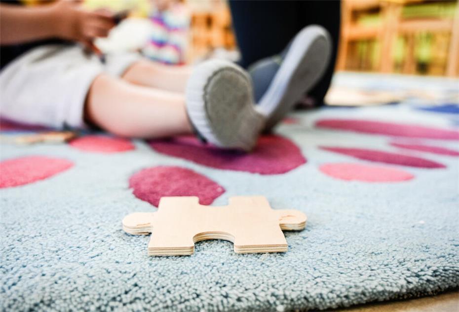 Ein Puzzleteil aus Holz liegt auf einem Teppich in einer Kita.
