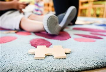 Ein Puzzleteil aus Holz liegt auf einem Teppich in einer Kita.