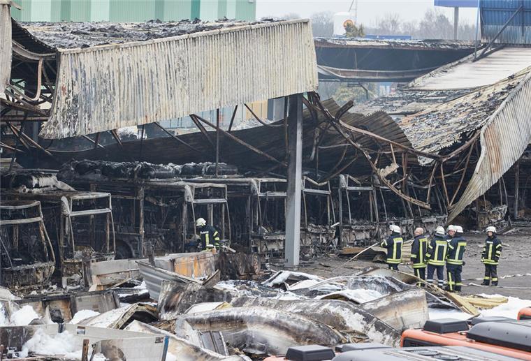 Feuerwehrmänner stehen auf dem von einem Brand zerstörten Gelände der Firma alga Nutzfahrzeug- und Baumaschinen GmbH.
