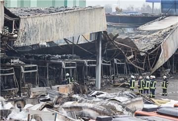 Feuerwehrmänner stehen auf dem von einem Brand zerstörten Gelände der Firma alga Nutzfahrzeug- und Baumaschinen GmbH.