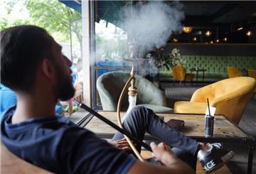 Ein Mann sitzt in einer Bar und pustet Rauch aus. Vor ihm steht eine Shisha.