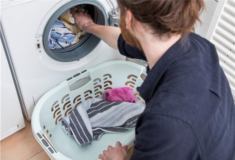Eine Person packt Wäsche in die Waschmaschine.