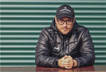 Mann mit schwarzer Jacke und Cappy vor einer grünen Wand. Benedetto Muzzicato hat seinen Job in Berlin verloren.
