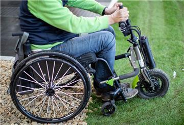 Ein Rollstuhl mit einem Zuggerät steht auf einer Rollstuhlteststrecke. „Triride“ ist ein leichtes Zuggerät, das an manuelle Rollstühle gekoppelt werden kann.