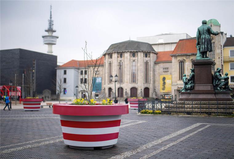 Ein rot-weiß gestreifter Kübel ist auf einem öffentlichen Platz zu sehen. 