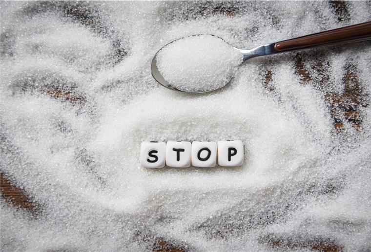 Eine Woche Verzicht auf den süßen Stoff Ein Haufen Zucker verstreut auf einem Tisch. Kleine Würfel bilden das Wort "Stop".