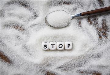 Ein Haufen Zucker verstreut auf einem Tisch. Kleine Würfel bilden das Wort "Stop". 