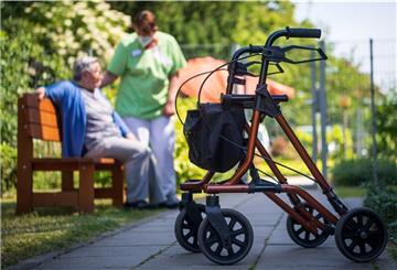 Ein Rollator steht nahe einer Pflegefachkraft und einer Bewohnerin eines Seniorenheims im Freien. 