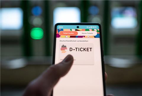 Ein Mann hält ein Mobiltelefon, auf dem das ·D-Ticket· gekauft werden kann