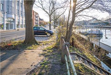 Blick auf die Kaistraße Bremerhaven mit Bootsanlegestelle und Parkplätzen neben Wohn- und Geschäftsgebäuden.