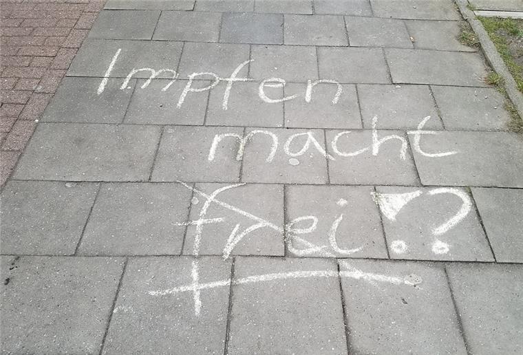 "Impfen macht frei" steht mit Kreide geschrieben auf einem Gehweg.