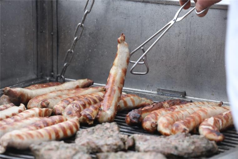 Bratwürste und anderes Fleisch liegen auf einem Holzkohlegrill. 