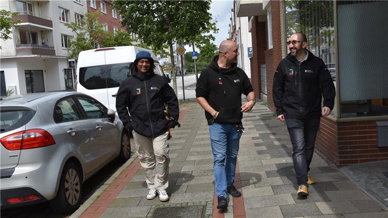 Drei Männer laufen nebeneinander auf dem Gehsteig und unterhalten sich dabei