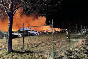 Auf einer eingezäunten Rasenfläche stehen brennende Fahrzeuge kurz nach Eintreffen der Feuerwehr.
