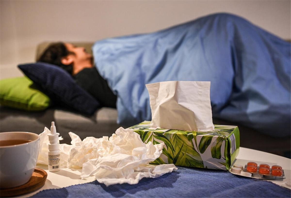 Magaluf-Grippe nach dem Urlaub: Rätselhafte Krankheit breitet sich aus Eine erkrankte Frau liegt am 16. Januar 2025 unter einer Decke zu Hause auf dem Sofa. Auf dem Tisch liegen Medikamente gegen Schnupfen und Erkältung - Nasenspray und Halstabletten - außerdem eine Tasse Tee und Taschentücher.