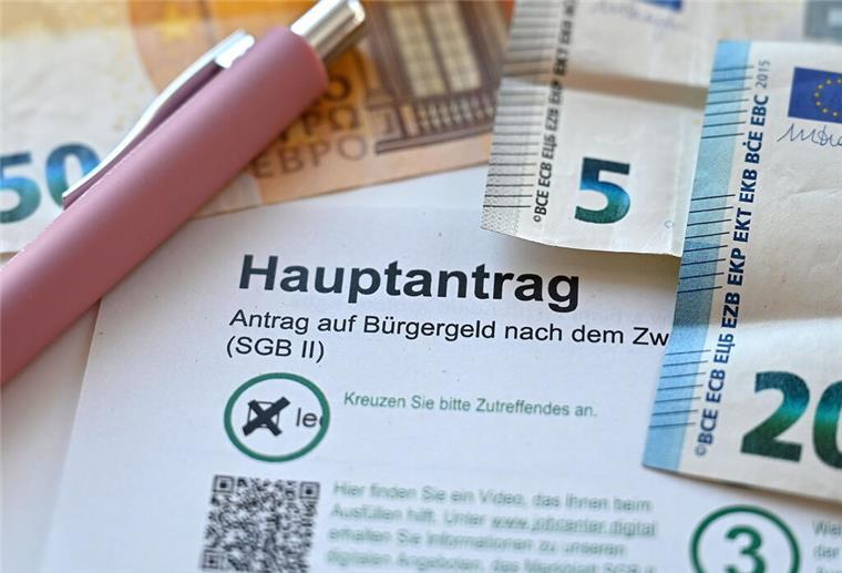 Der Hauptantrag für Bürgergeld liegt neben Geldscheinen auf einem Tisch. 