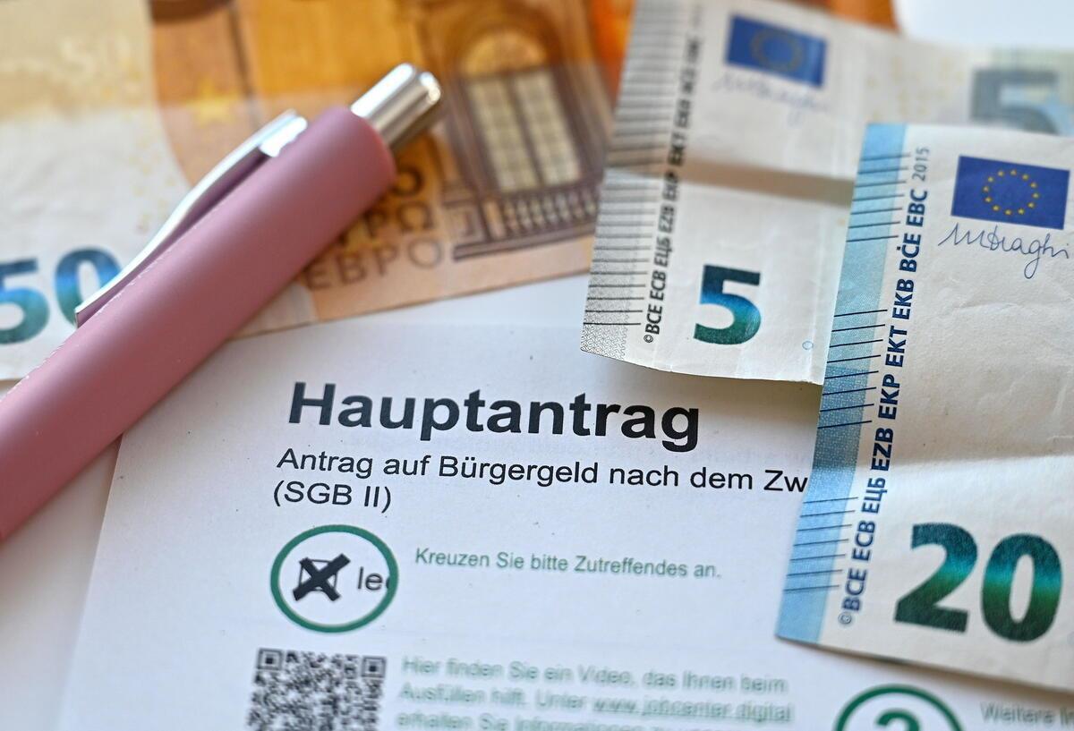 Bürgergeld 2025: Neue Sanktionen für Pflichtverletzung kommen Der Hauptantrag für Bürgergeld liegt neben Geldscheinen auf einem Tisch.
