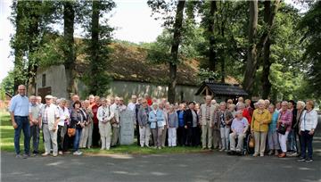Bürgermeister und Reiseführer Norbert Wolf (links) mit den Senioren unter den Eichen von Brümmerhof. Das Fleckchen hatte beim Kreisentscheid 2017/18 „Unser Dorf hat Zukunft“ die Siegerurkunde errungen. Eine Infotafel informiert, dass hier heute elf Wohnhäuser, davon sechs Hofstellen, eine im Vollerwerb, angesiedelt sind.  