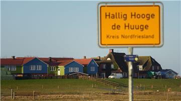 Bunte Häuser sind auf einer Warft auf Hallig Hooge hinter dem Ortsschild zu sehen.
