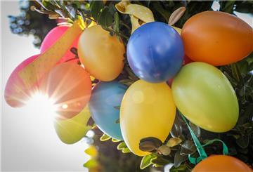 Bunte Plastikostereier hängen bei Sonnenschein an einem Gesteck.