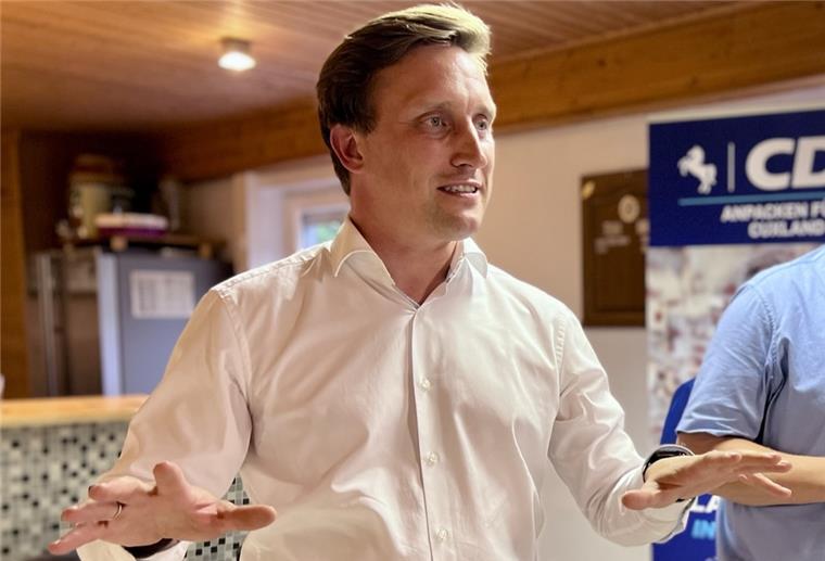 Ein Mann mit weißem Hemd gestikuliert mit beiden Händen, daneben steht ein Mann mit blauem Hemd, der die Hände vor dem Bauch verschränkt. 
