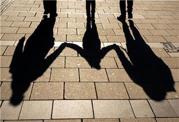  Die Schatten von zwei Erwachsenen und einem Kind fallen in den Morgenstunden auf den Asphalt. 