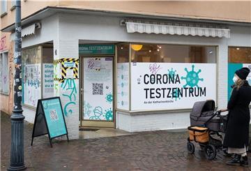 Eine Frau mit Kinderwagen steht vor einem Corona - Testzentrum, das in einem Eckhaus untergebracht ist. 