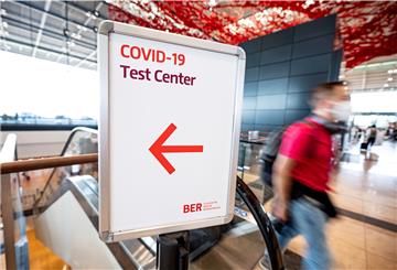 Fluggäste laufen durch die Haupthalle des Flughafens Berlin Brandenburg (BER) an einem Schild mit der Aufschrift "Covid-19 Test Center" vorbei. 