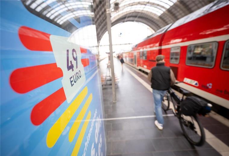Ein Mann geht am Frankfurter Hauptbahnhof mit seinem Fahrrad zwischen der Werbung für das Deutschlandticket und einer Regionalbahn entlang.