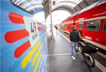 Ein Mann geht am Frankfurter Hauptbahnhof mit seinem Fahrrad zwischen der Werbung für das Deutschlandticket und einer Regionalbahn entlang.