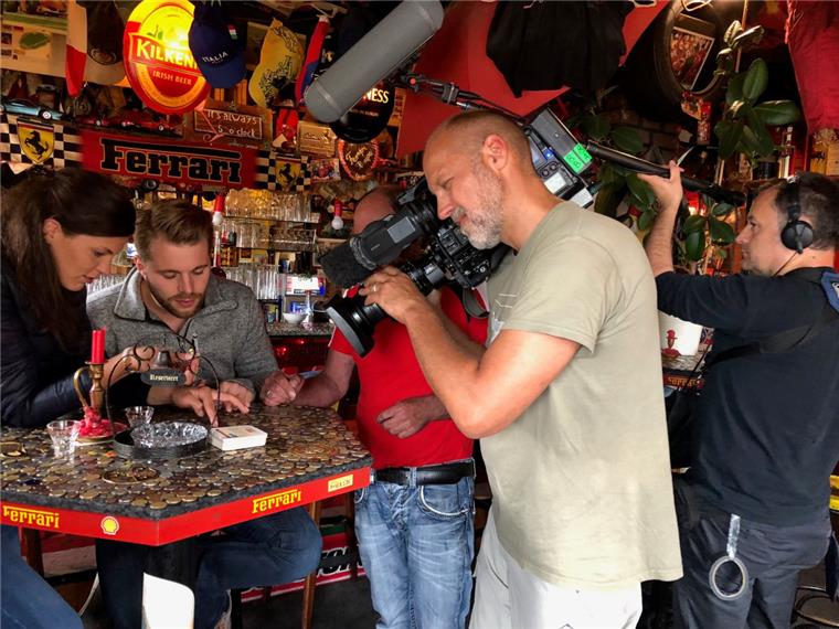 Das Doku-Protagonisten-Pärchen, Indra Uihlein und Jonas Dülberg hat, wie so viele Gäste vor ihnen, Münzen auf den Kneipentisch geklebt. Im Vordergrund sind Kameramann Grischa Kerstan und Tonassistent Mathias Onken zu sehen. Dahinter (verdeckt) Gastwirt Hans Sauerbrei.