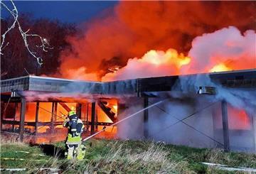 Brennendes Gebäude mit lodernden Flammen, zwei Feuerwehrleute versuchen, das Feuer zu löschen