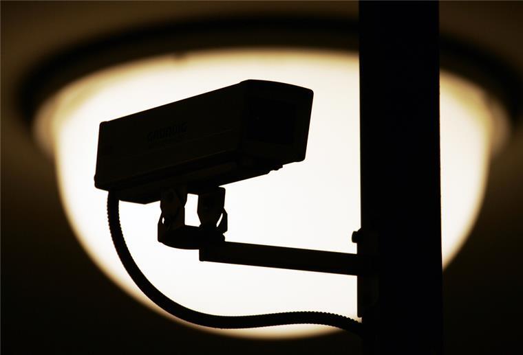 Eine Video-Überwachungskamera zeichnet sich vor einer Lampe in einem S- und U-Bahnhof als dunkle Silhouette ab.