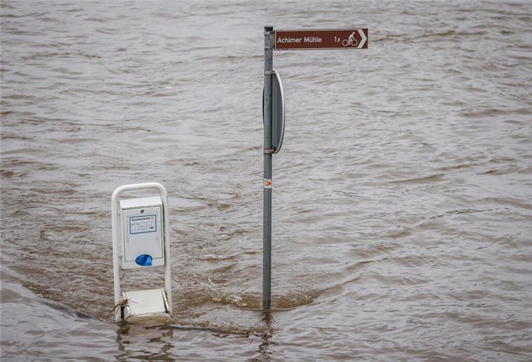Das Hochwasser der Weser umströmt einen Wegweiser in Achim.