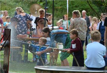 Kinder spielen in einem Stadtpark bei einem Fest mit einem Wasserschlauch.