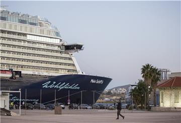 Kreuzfahrtschiff liegt hinter einem Zaun an einer Kaje. Im Vordergrund ein Mensch. 