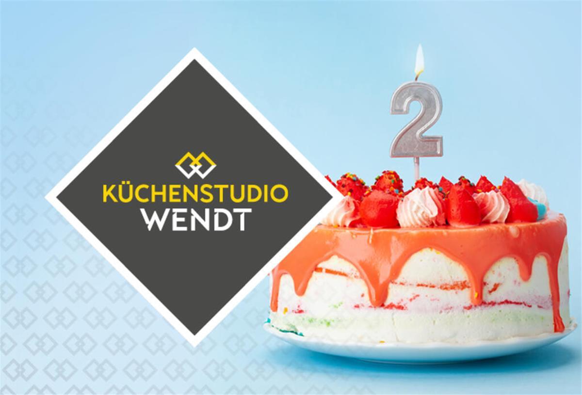 Küchenstudio Wendt: Zweiter Geburtstag mit Angeboten und buntem Programm Eine Erdbeer-Geburtstagstorte mit einer Zwei und einer Kerze steht neben dem Logo vom Küchenstudio Wendt