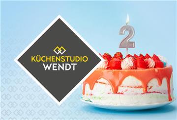 Eine Erdbeer-Geburtstagstorte mit einer Zwei und einer Kerze steht neben dem Logo vom Küchenstudio Wendt
