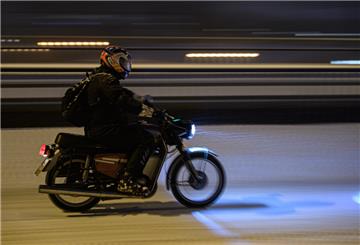Ein Mann fährt mit einem Moped bei Schneefall über eine verschneite Straße in der Innenstadt. 