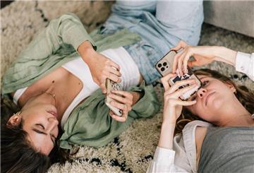 Zwei junge Frauen liegen auf dem Rücken und schauen in ihre Handys.
