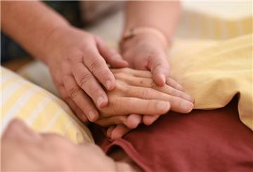 Eine Hospizmitarbeiterin hält die Hand eines todkranken Menschen