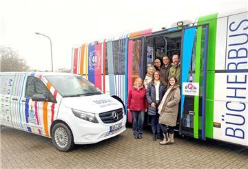 Das Team der Fahrbücherei im Eingang des Bücherbusses. Vor ihnen steht das neue Elektrofahrzeug. 