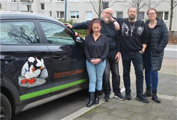 Zwei Frauen und zwei Männer posieren vor einem schwarzen Fahrschulauto.