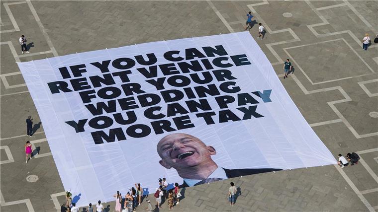 Krieg bringt Hochzeitspläne von Bezos durcheinander Das Transparent zeigt ein Foto des Amazon-Gründers, auf dem steht: „If you can rent Venice for your wedding you can pay more tax“.