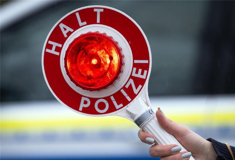  Das Logo der Polizei auf der Dienstkleidung von Polizisten die vor einem Blaulicht stehen 