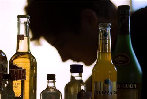 Ein Jugendlicher sitzt hinter Flaschen mit Alkohol,