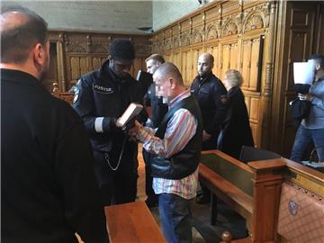 Der Angeklagte wird von der Polizei in den Gerichtssaal geführt, wo ihm dann die Handschellen abgenommen werden.
